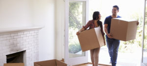 Woman and man walking into empty house carrying boxes